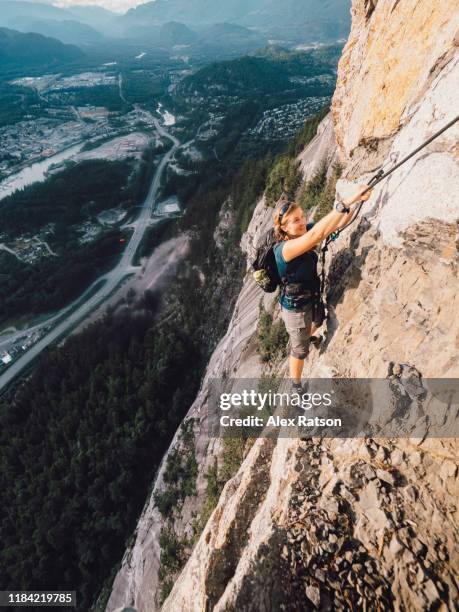 a young women traverses across an exposed ledge while rock climbing on the stawamus chief - beautiful perfection exposed lady imagens e fotografias de stock