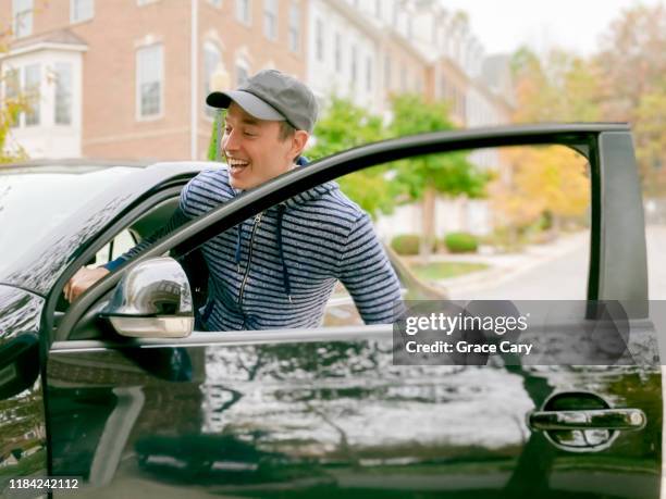 man smiles while entering car - entering photos et images de collection