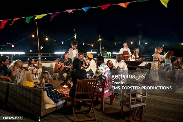 large group of friends sitting together and enjoying a summer urban rooftop party in munich - party in munich stock pictures, royalty-free photos & images
