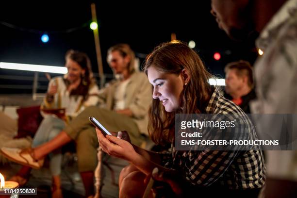 young female student is using her mobile phone on a urban rooftop summer party - social influencer stock pictures, royalty-free photos & images
