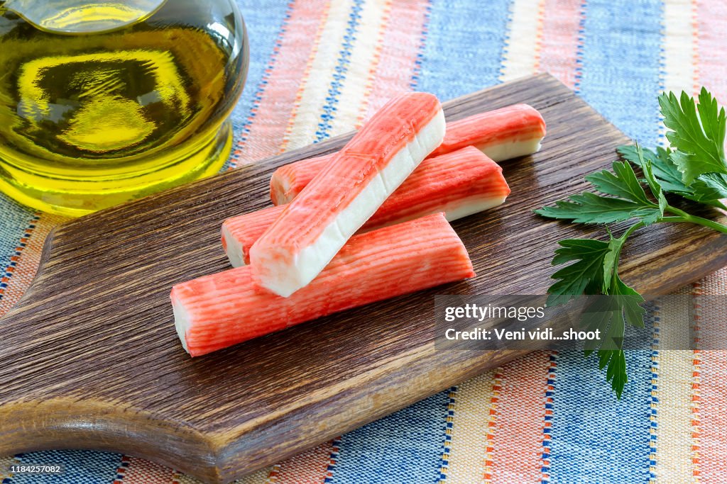 Surimi krab stokken en peterselie op een bruin snijplank in de buurt van jar met olijfolie. Zeevruchten en ingrediënt voor salades. Gezond eten en koken thuis.