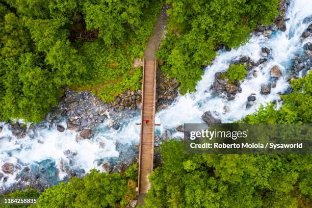 hiker crossing river towards mardalsfossen waterfall, norway - green bridge over trees stock pictures, royalty-free photos & images