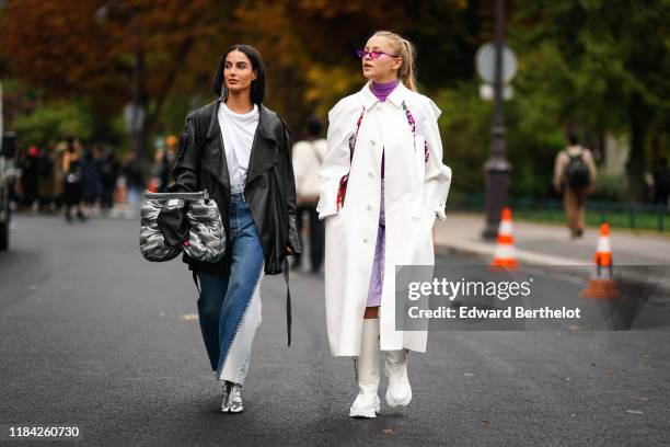 Fiona Zanetti wears earrings, a white top, a black leather oversized jacket, a lustrous grey Glam Slam clutch, blue denim patchwork pants, shiny...