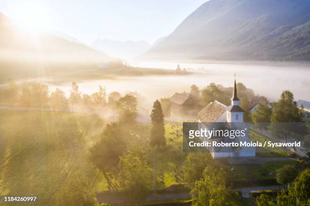 fog over church of stryn at sunrise, norway - olden norwegen stock-fotos und bilder