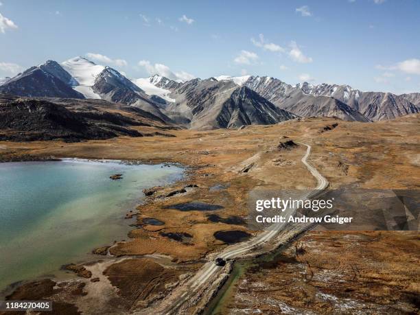 drone shot of toyota 4runner with rooftop box driving across vast valley with glacier snow capped majestic mountains in distance. - kyrgyzstan stock pictures, royalty-free photos & images