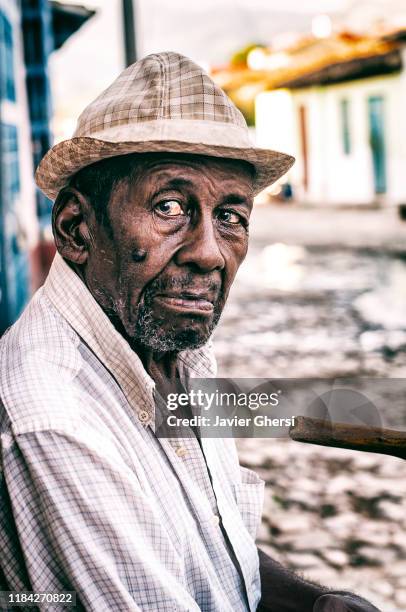 hombre anciano con sombrero sentado en la puerta de su casa. trinidad, cuba. - hombre sentado stockfoto's en -beelden