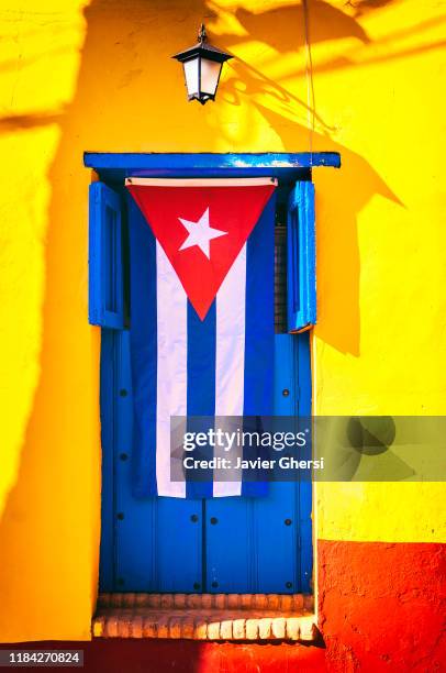 bandera cubana sobre una ventana azul y pared amarilla. trinidad, cuba. - bandera cubana stock pictures, royalty-free photos & images