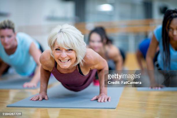 donna anziana in classe fitness in una posa plank foto d'archivio sorridente - sportiva foto e immagini stock