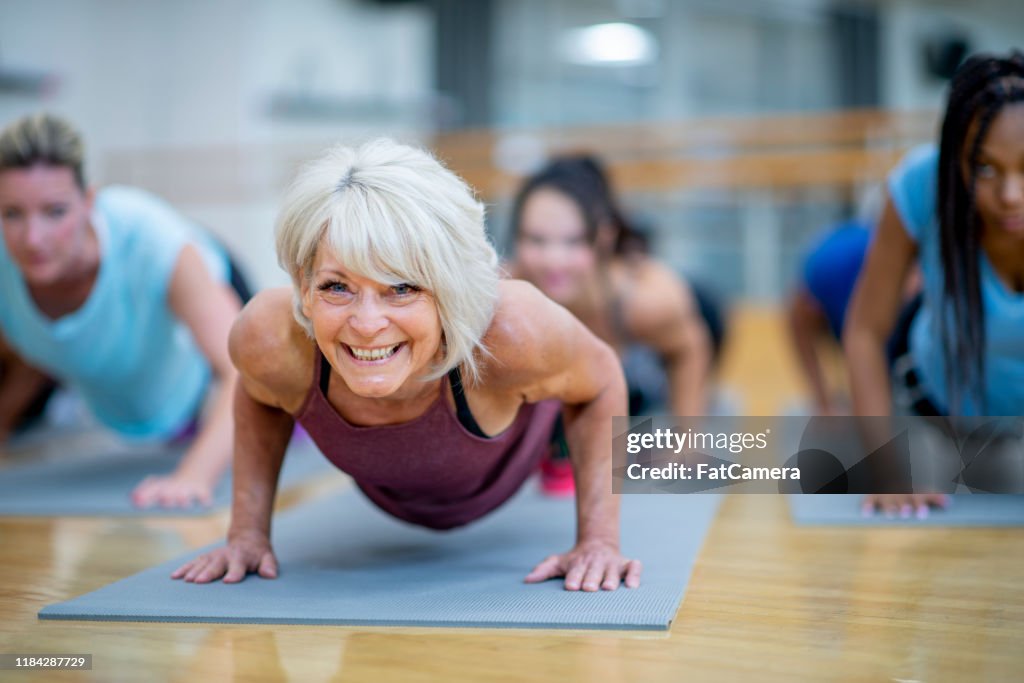 Mulher sênior na classe da aptidão em uma foto conservada em estoque de sorriso do pose da prancha