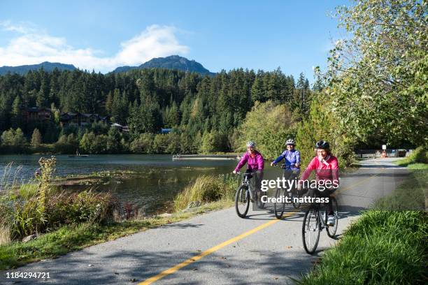 aktive senioren radeln auf einem gepflasterten weg in der nähe des sees - trail britisch kolumbien stock-fotos und bilder
