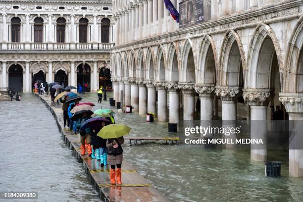 People walk on a footbridge across a flooded waterfront on November 24, 2019 in Venice during a high tide "Acqua Alta" meteorological phenomenon with...