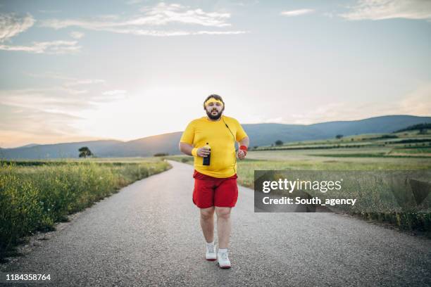 übergewichtiger mann joggt bei sonnenuntergang auf der straße - chubby men stock-fotos und bilder