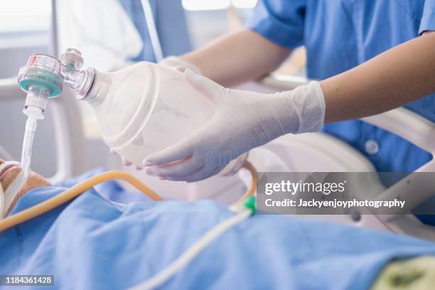 doctor holding oxygen ambu bag over patient given oxygen to patient by intubation tube in icu/emergency room - hospital ventilator ストックフォトと画像