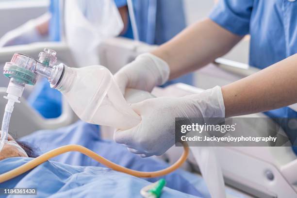 doctor holding oxygen ambu bag over patient given oxygen to patient by intubation tube in icu/emergency room - équipement d'assistance respiratoire photos et images de collection