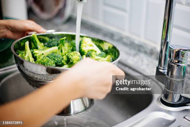 woman washing broccoli in the kitchen sink - brocolli stock pictures, royalty-free photos & images