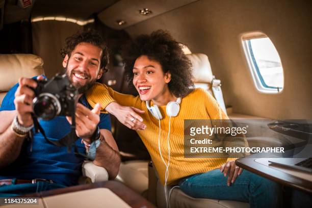 romantisch multi-etnisch stel kijkend naar foto's op een dslr-camera samen tijdens het reizen aan boord van een privé-jet - couple airplane stockfoto's en -beelden