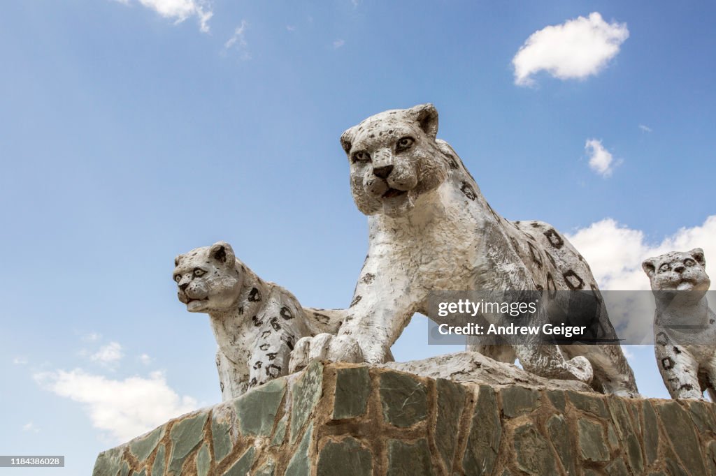 Concrete statues of snow leopards on monument with puffy white cloud filled sky.