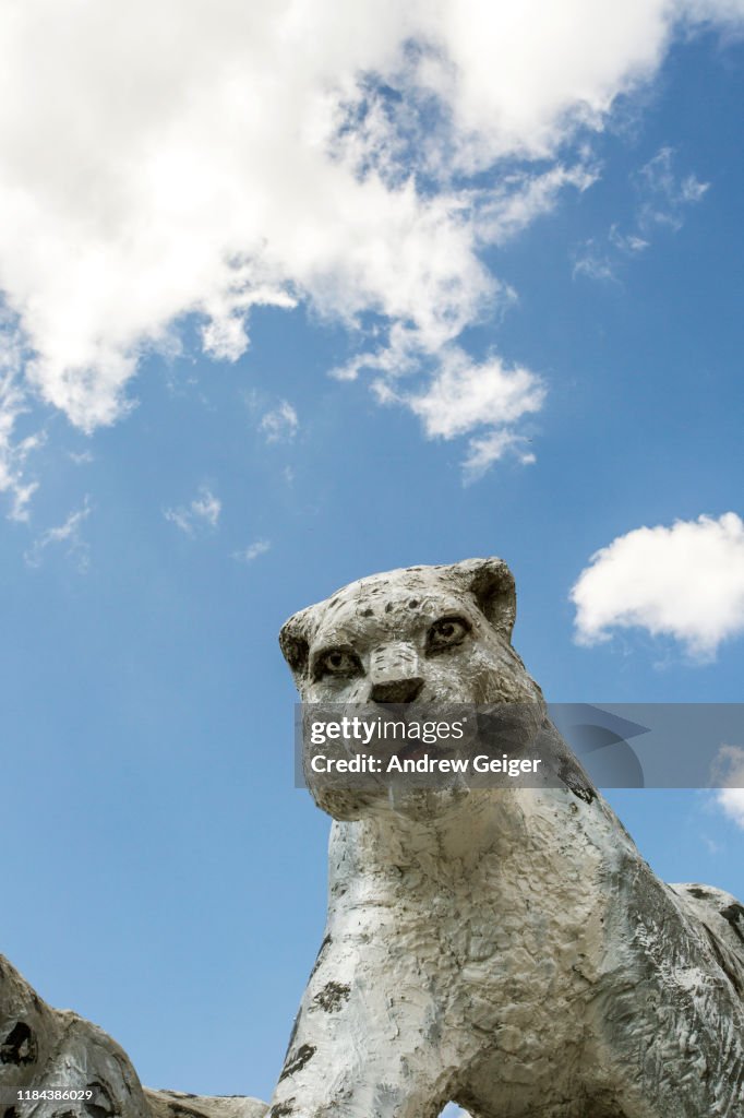 Concrete statues of snow leopards on monument with puffy white cloud filled sky.