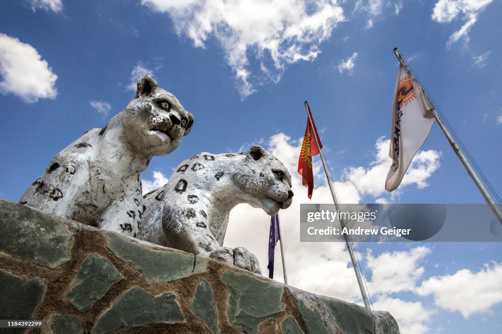 Concrete statues of snow leopards on monument with Kyrgyzstan flags and puffy white cloud filled sky.