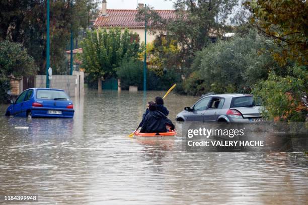 People ride on a small boat next to partially submerged cars on a flooded street after heavy rains in Le Muy, southeastern France, on November 24,...