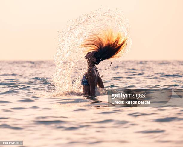 beautiful woman doing a water spin with her hair in the ocean during sunset - asian water splash stock-fotos und bilder