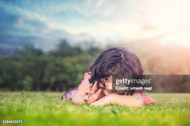 smiling little cute baby girl lying on the grass in the park - cute indian girls stock pictures, royalty-free photos & images