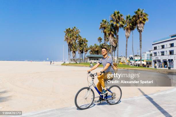 young happy smiling man riding a bike at venice beach, los angeles, california - la waterfront stock pictures, royalty-free photos & images
