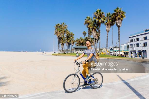 young happy smiling man riding a bike at venice beach, los angeles, california - la waterfront 個照片及圖片檔