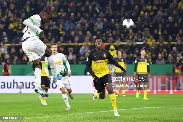 Marcus Thuram of Borussia Monchengladbach scores his team's first goal as Dan-Axel Zagadou of Borussia Dortmund looks on during the DFB Cup second...