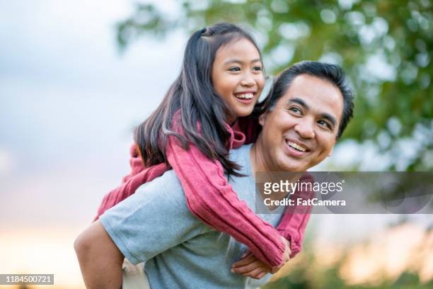 father giving his daughter a piggyback ride stock photo - father stock pictures, royalty-free photos & images