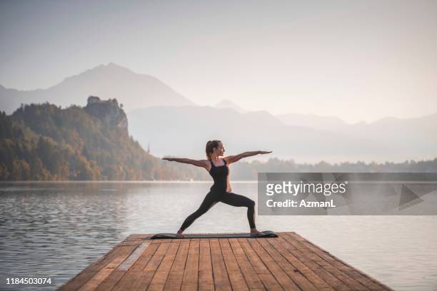 young woman in warrior ii position overlooking lake bled - yoga stock pictures, royalty-free photos & images