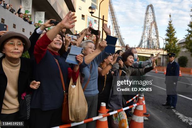 People wave as they see the motorcade of Pope Francis pass by on his way to the Tokyo Dome stadium for a holy mass, in Tokyo on November 25, 2019.