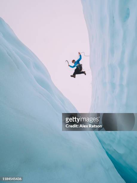 mountaineer jumps over large crevasse - winter sport stock-fotos und bilder