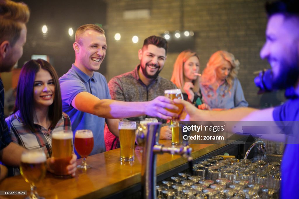 Smiling young man taking a glass of beer from the bartender