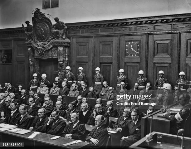 Nazi Defendants sit in the dock behind their legal counsel, under guard in Room 600 at the Palace of Justice in Nuremberg during legal proceedings...