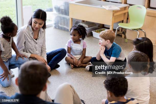 diverse children and teachers sit in circle and play game - children circle floor stock pictures, royalty-free photos & images