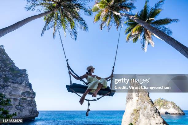 female tourist playing bali swing at nusa penida island, indonesia. - indonesian girl stock pictures, royalty-free photos & images