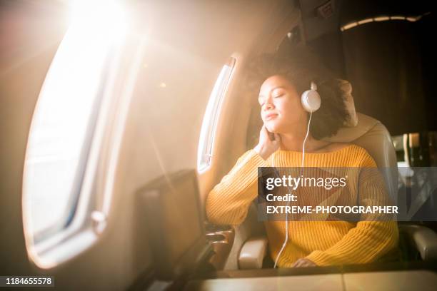 young fashionable woman sitting in a private jet and listening to music through the headphones - voyage zen stock pictures, royalty-free photos & images