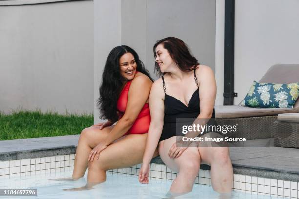 two mid adult women sitting on outdoor swimming poolside chatting and laughing together, cape town, south africa - full figure stock pictures, royalty-free photos & images