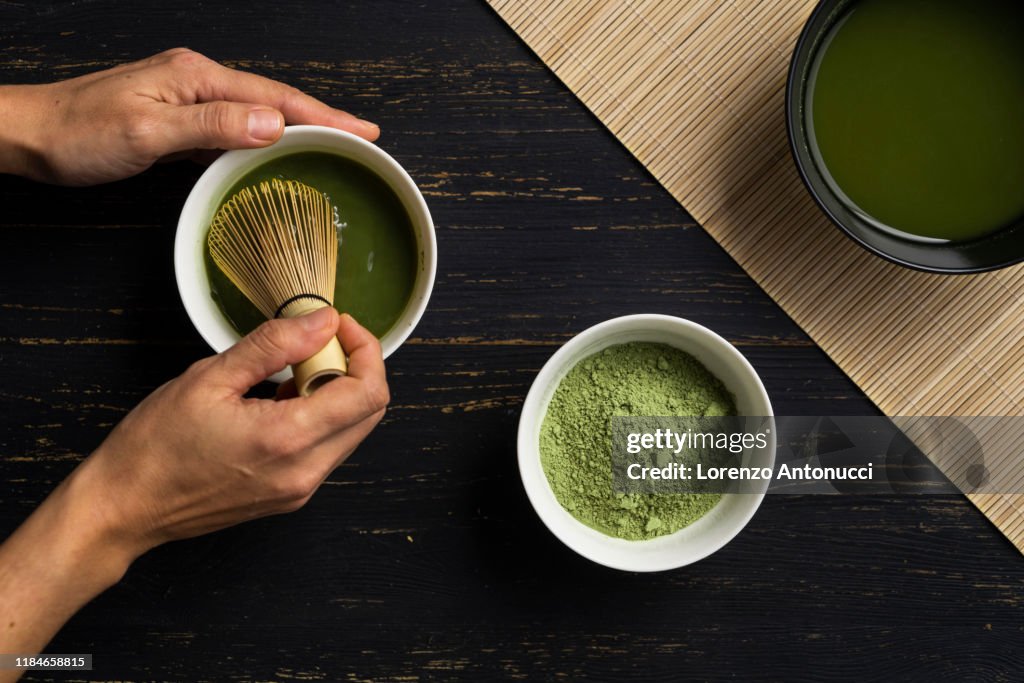 Woman's hands mixing matcha green tea powder in a bowl, overhead view