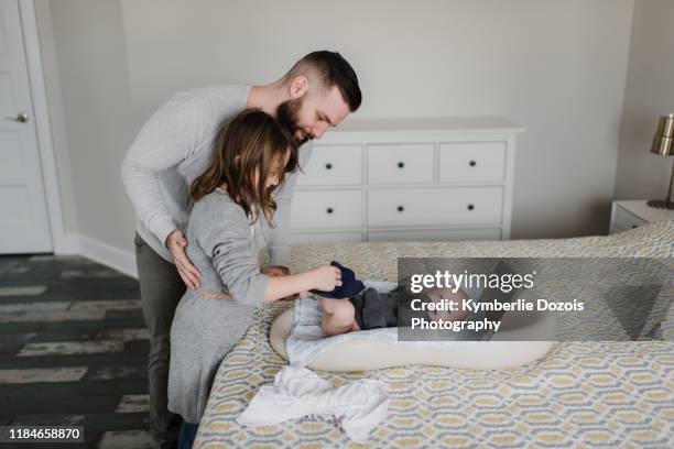 girl with father changing baby brother's diaper on bed, side view - sibling support stock pictures, royalty-free photos & images