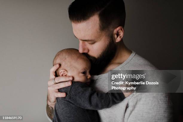 young man kissing baby son on head, head and shoulders - genderblend stock-fotos und bilder