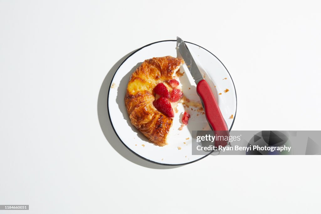 Strawberry danish pastry on plate with swiss army knife, overhead view