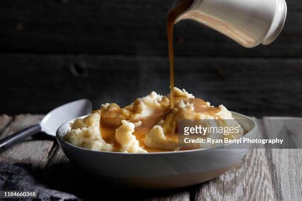 jug of gravy being poured onto bowl of steaming mashed potatoes, studio shot - pour over stock pictures, royalty-free photos & images