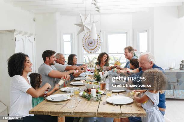 family popping christmas crackers together at dining table - christmas family stock-fotos und bilder