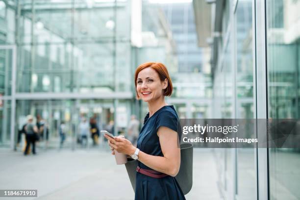 side view portrait of young businesswoman with coffee and smartphone outdoors in city. - portrait outdoor business foto e immagini stock