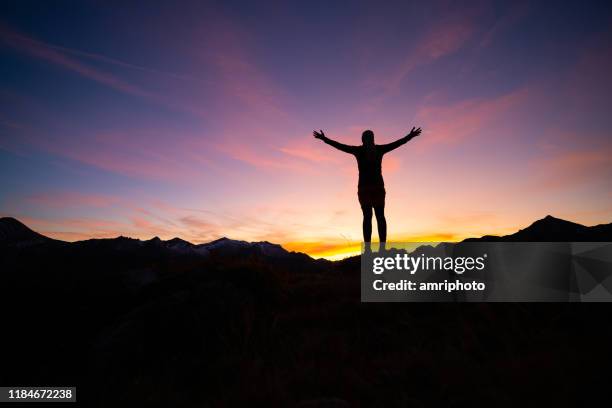 silhouette of sporty woman standing high up in mountains at sunset with open arms - arms outstretched silhouette stock pictures, royalty-free photos & images