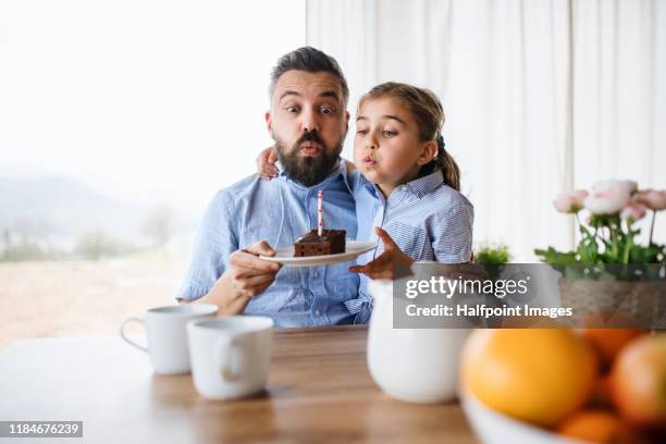 small girl and her father indoors at home, blowing candle on cake. - man giving cake candle stock pictures, royalty-free photos & images