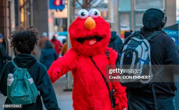 Person dressed as "Sesame Street" character Elmo greets people on 42nd Street on November 4, 2019 in New York. - Beneath flashing billboards and...