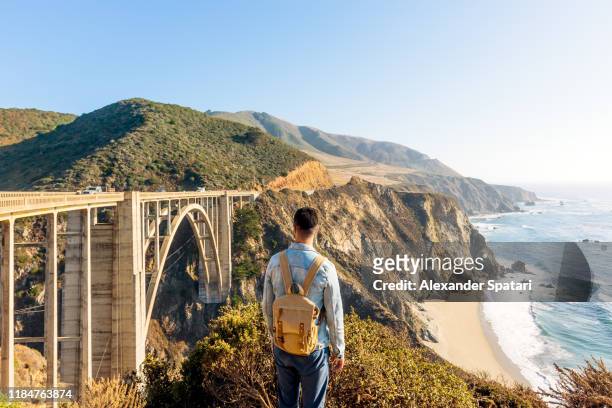 rear view of a man with backpack looking at bixby bridge in california, usa - bixby creek bridge stock pictures, royalty-free photos & images
